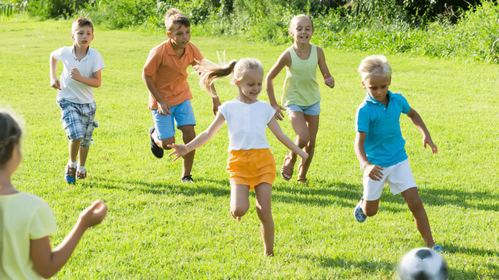 Jongens en meisjes van ongeveer 10 jaar oud die op een grasveld rennen en voetbal spelen